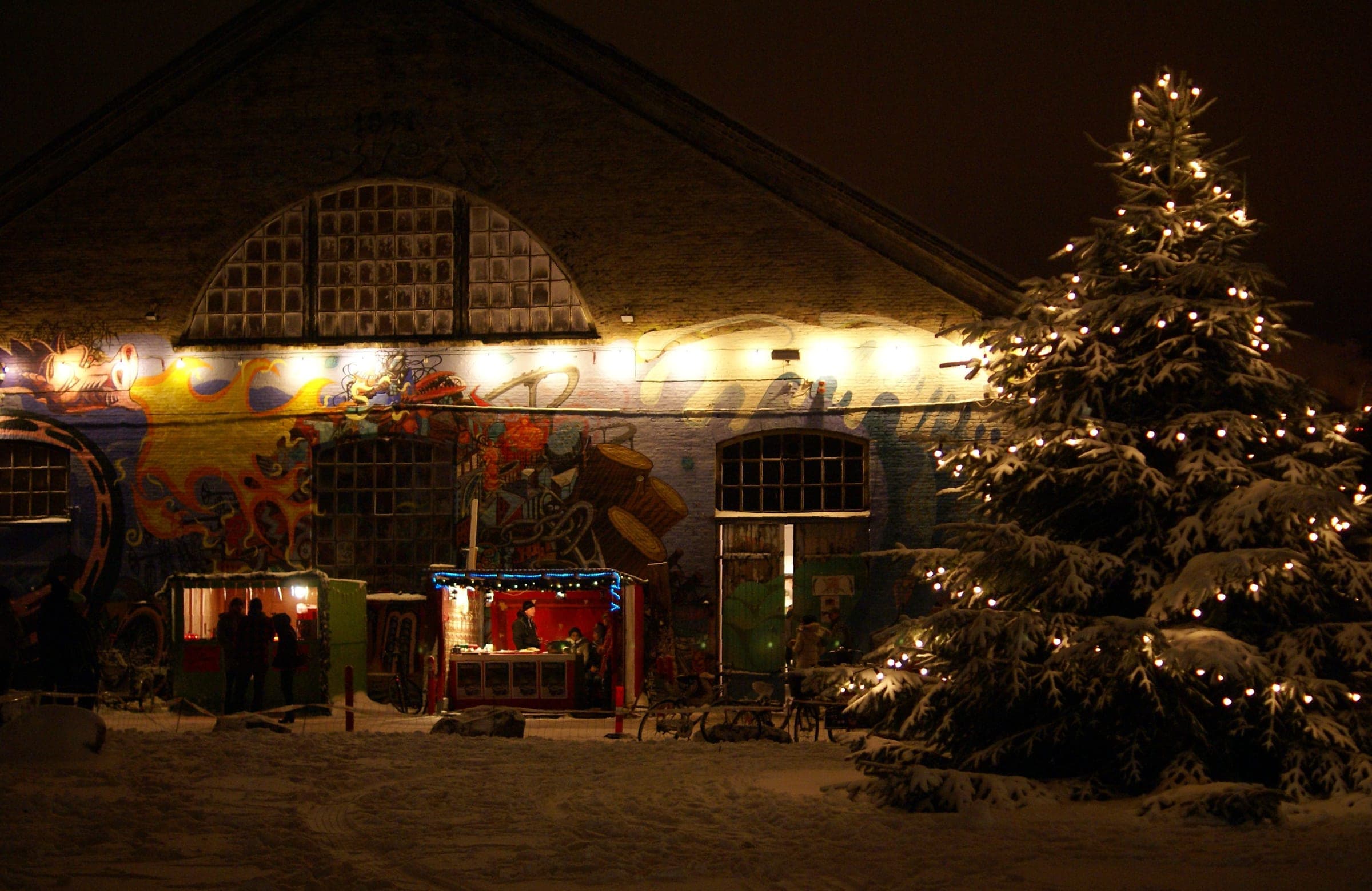 A lit Christmas tree stands in the snow outside the painted front of Den Grå Hal in Christiania in Copenhagen.