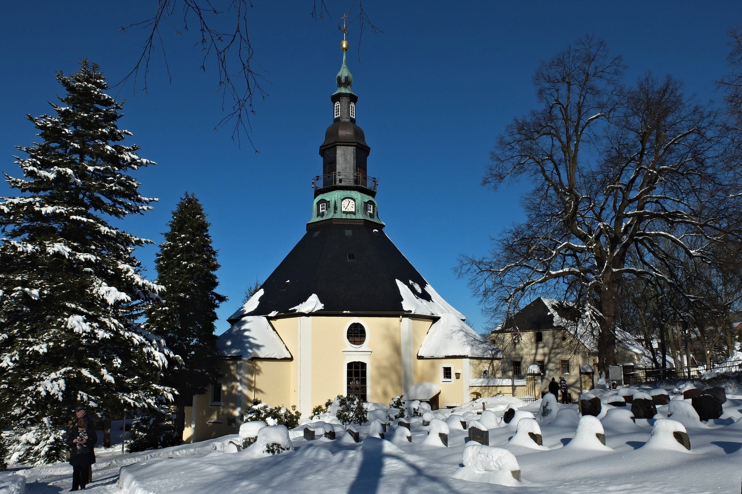 Deep snow covers the churchyard around the eight-sided Bergkirche in Seiffen under a clear winter sky.