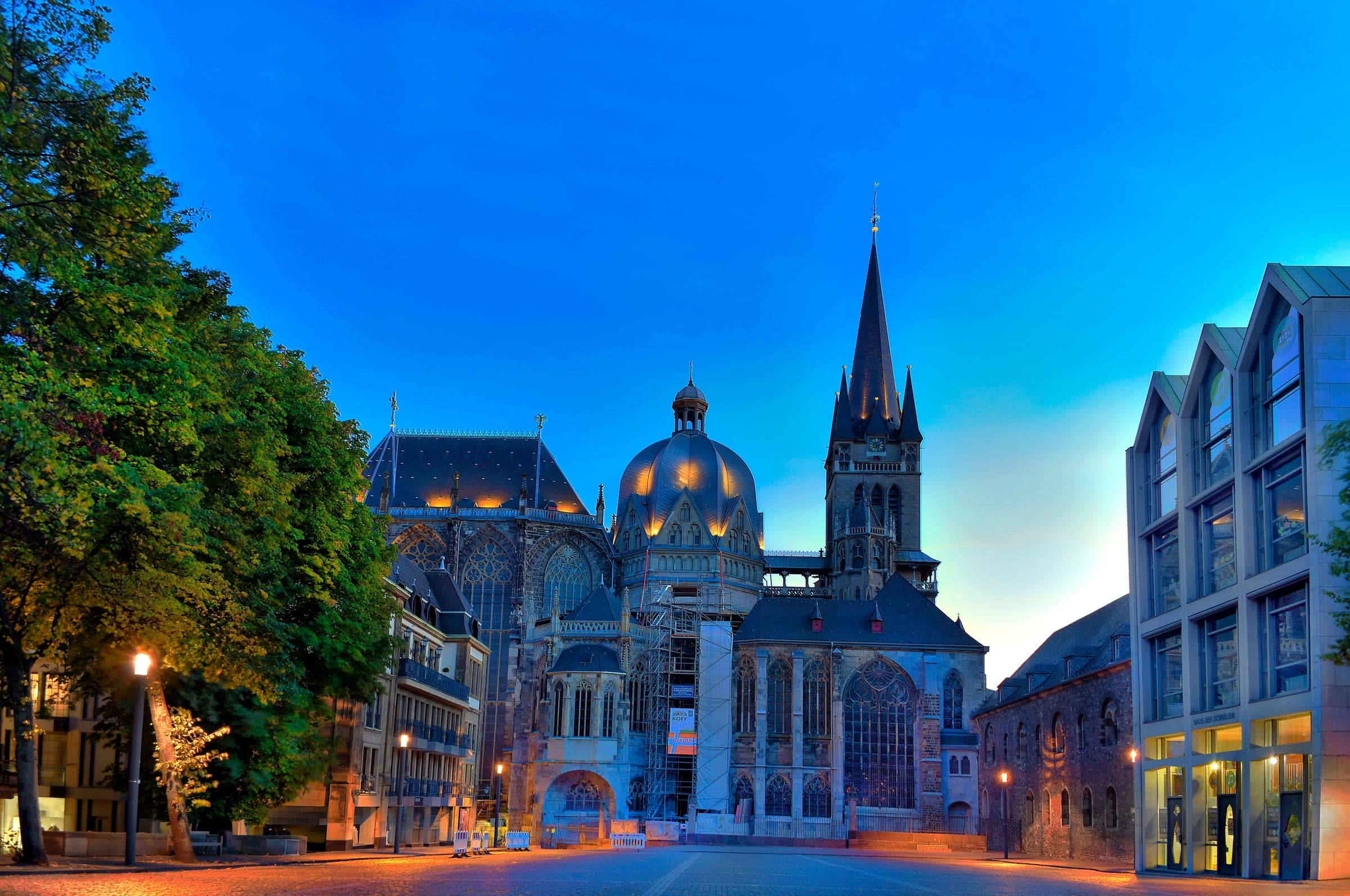 Lamps light the dome and Gothic tower of Aachen Cathedral at blue hour